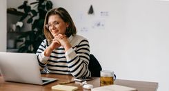 Woman smiling thoughtfully at her desk with a laptop, representing a nonprofit founder planning her next steps.